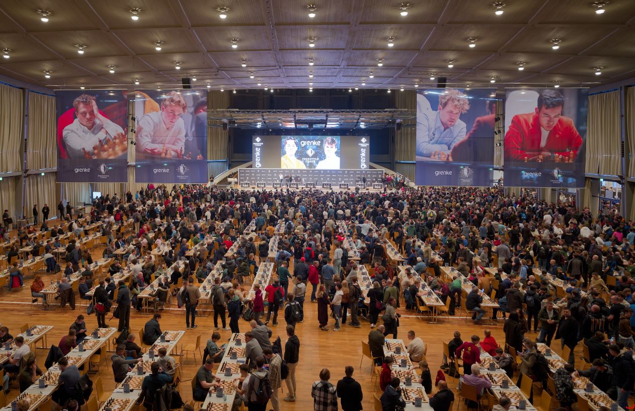 Wide view of the GRENKE Chess Open playing hall in Karlsruhe, rows of boards and players under Freestyle Chess and sponsor banners